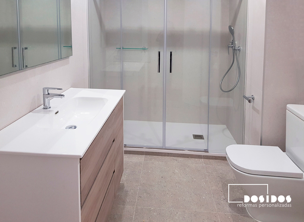 Baño espacioso y luminosa con mueble madera clara, ducha extraplana grande, mampara corredera transparente e inodoro.