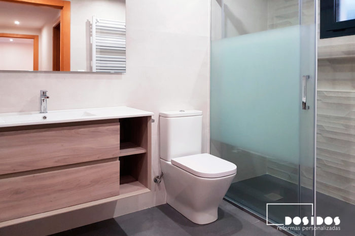 Reforma de baño con un mueble de baño en madera pino gris, con dos cajones, inodoro y ducha con mampara corredera.