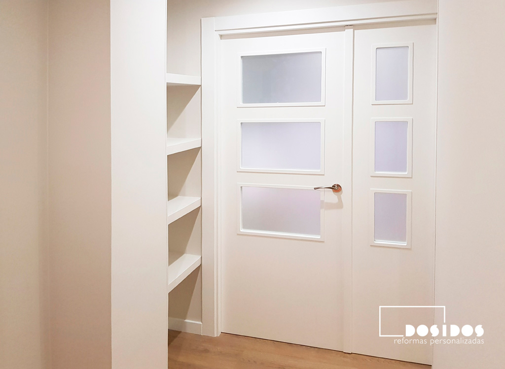 Recibidor con estantería de escayola decorativa para disimular un pilar y puerta doble entrada al salón vidriera blanca.