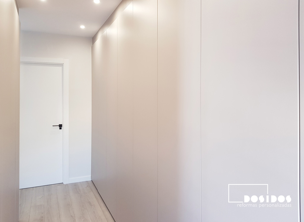 Armario vestidor cerrado con puertas abatibles lisas color cachemir, suelo parquet y puerta del baño al fondo color blanco.