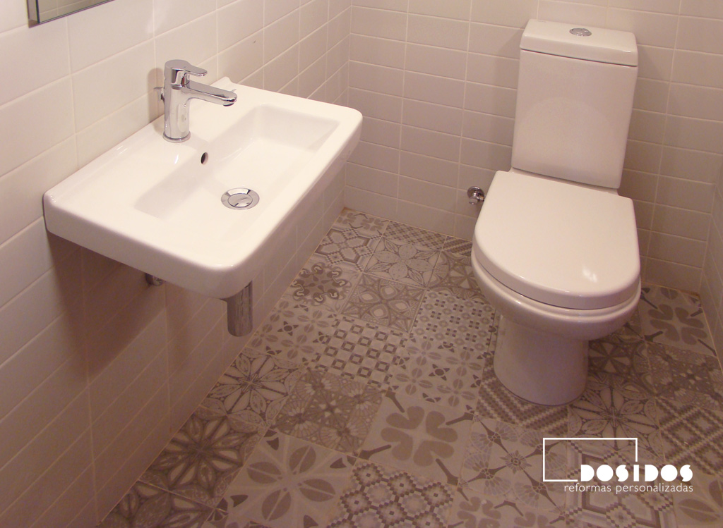 Baño pequeño con un lavabo de porcelana pequeño suspendido, inodoro y azulejos grises con dibujos en el suelo de vives cerámica.