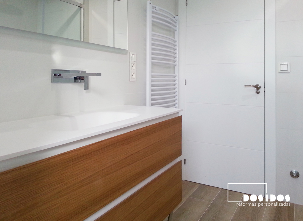 Baño alicatado blanco, mueble de madera dos cajones lavabo krion y grifo a pared.