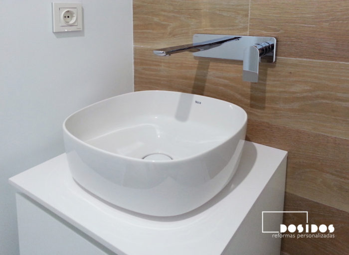 Detalle del lavabo de porcelana sobre un mueble y grifo a pared en un baño pequeño.