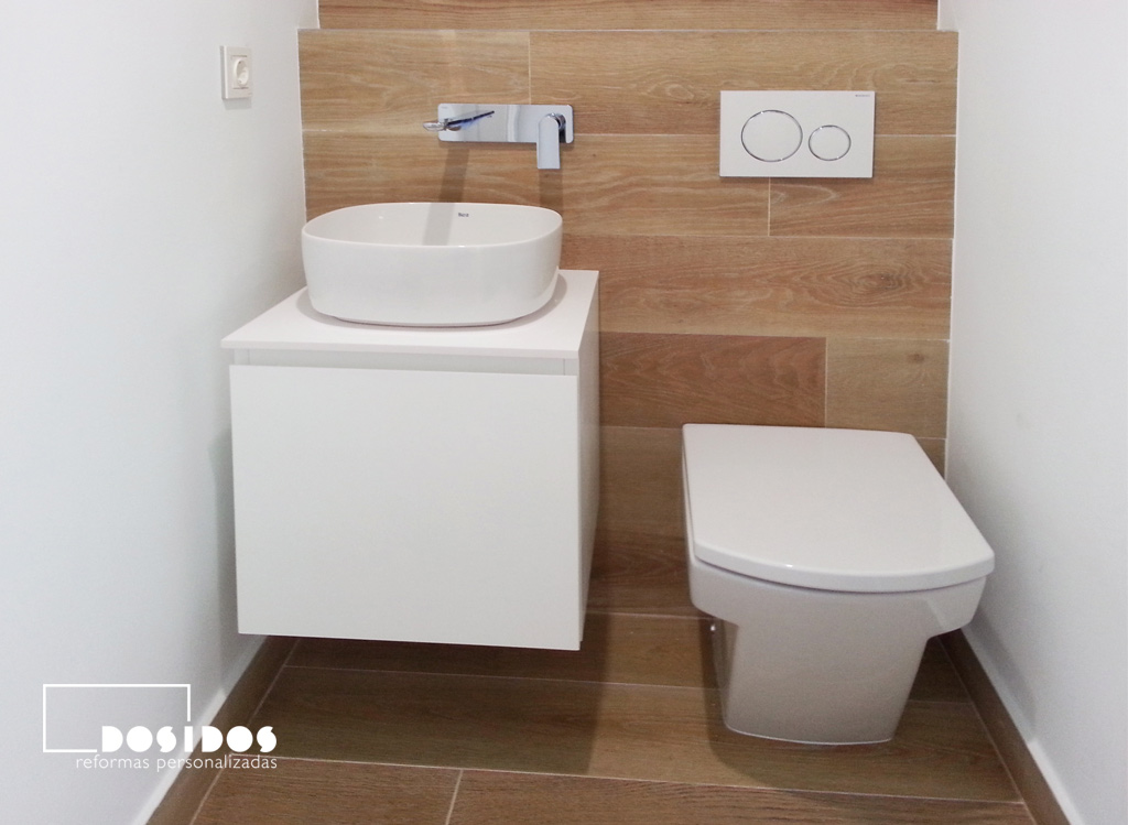 Un baño pequeño, detalle del lavabo sobre un mueble, grifo a pared e inodoro empotrado.