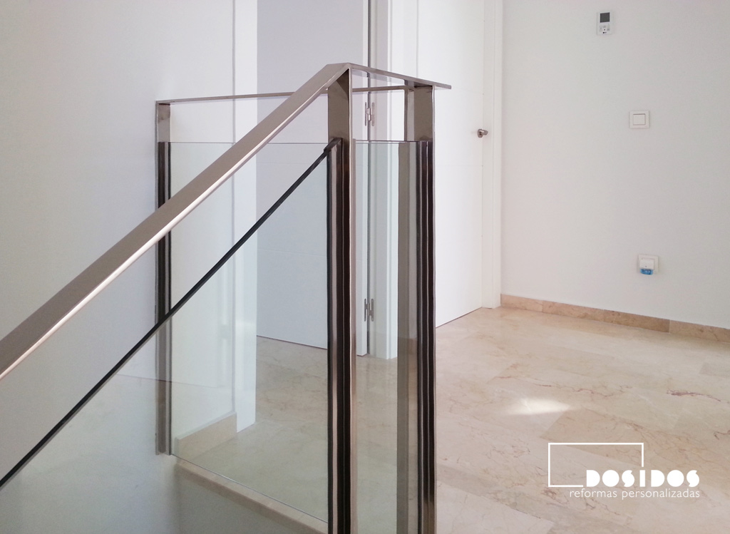 Detalle de una barandilla de escalera, fabricada a medida en pletina de acero inoxidable y cristal transparente.