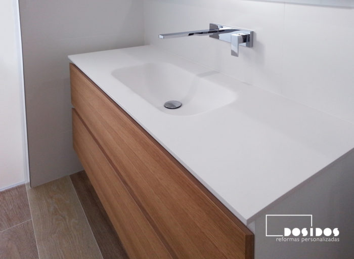 Mueble de baño con 2 cajones de madera y laterales lacados en blanco, un lavabo de krion con grifo empotrado a pared.