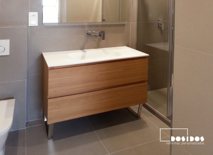 Reforma baño moderno con mueble de madera, lavabo de krion y grifo empotrado a pared.