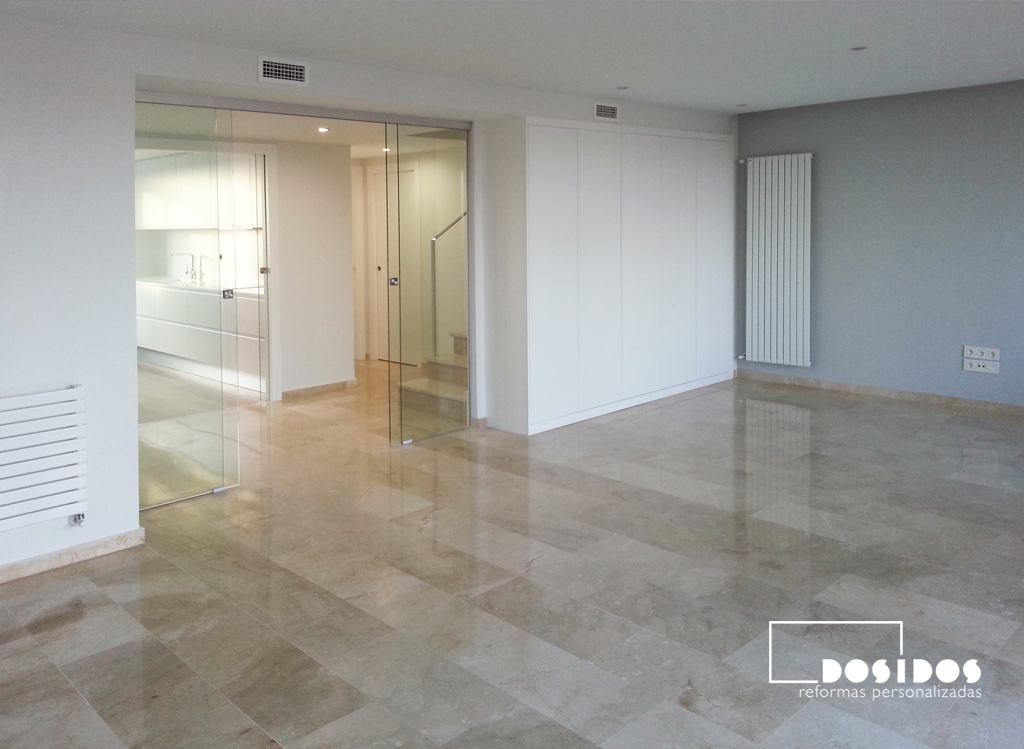 Gran salón con puerta corredera de cristal transparente, suelo de mármol pulido, armario lacado y radiador diseño vertical.